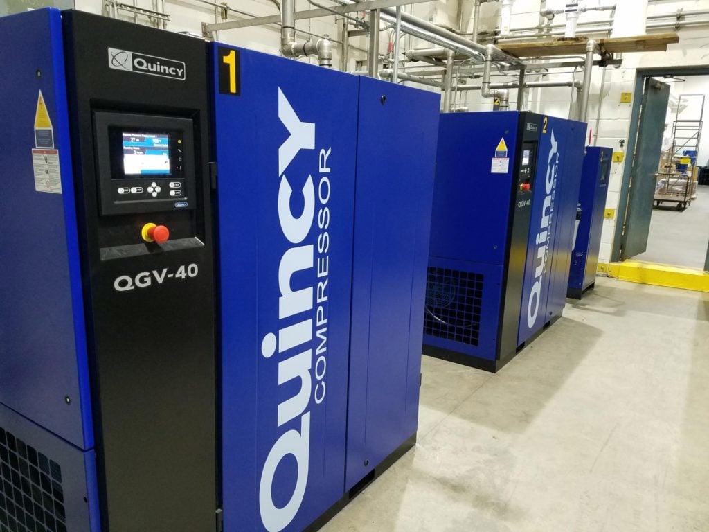 3 blue quincy compressors in a line on a factory floor